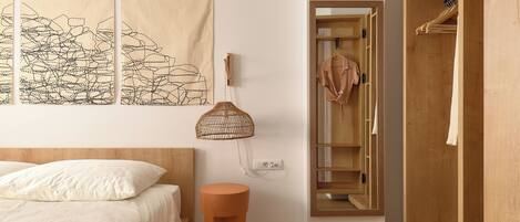 A bedroom with a bed, a bedside table, a hanging lamp, a wardrobe, and a wall-mounted phone.