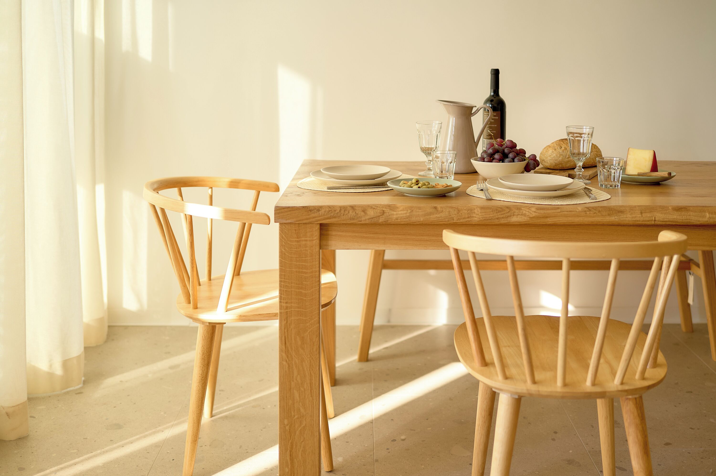 Una mesa de madera con platos, vasos, una botella y un bol de uvas.