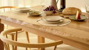 Une table de salle à manger en bois, avec des assiettes, des bols, un pichet, une bouteille et une miche de pain.