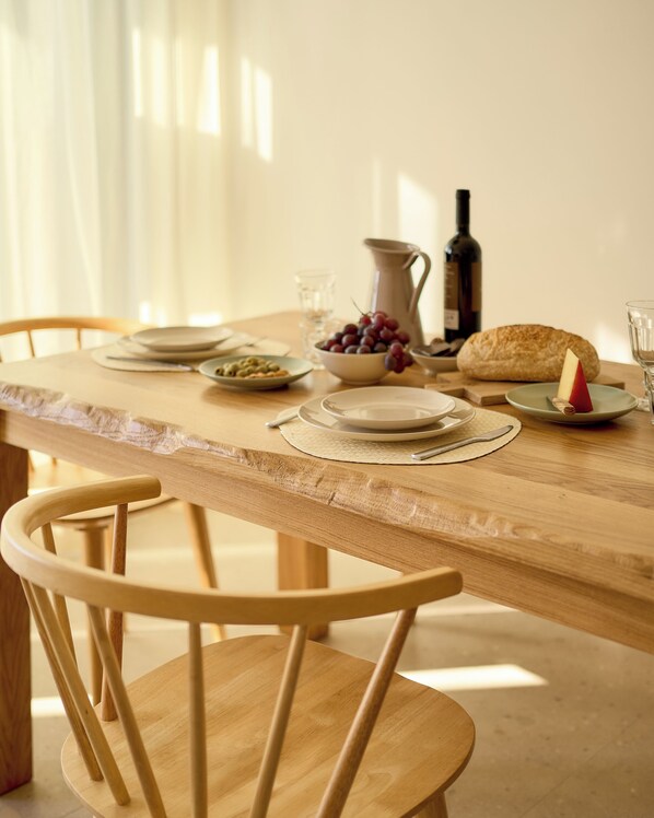 A wooden dining table with plates, bowls, a pitcher, a bottle, and a loaf of bread.