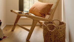 Une chaise en osier avec un coussin, un panier tressé et une fenêtre donnant sur un paysage verdoyant.