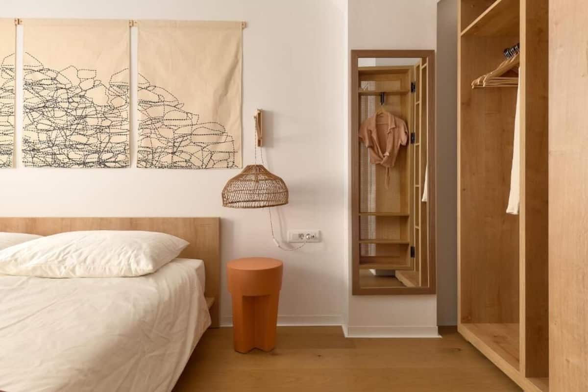 A bedroom with a bed, a round stool, a hanging lamp, a wardrobe, and a closet with clothes.