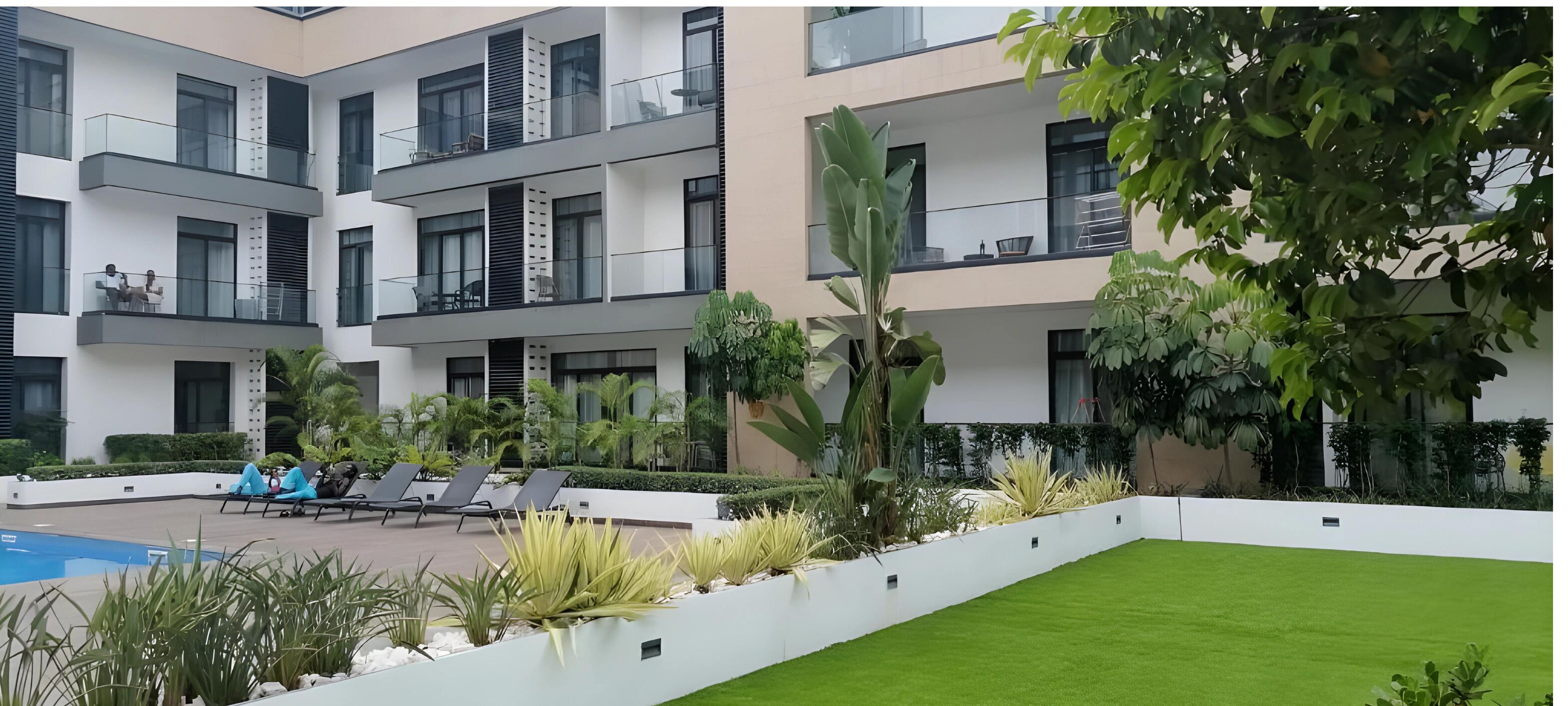 Un immeuble résidentiel à plusieurs étages, doté de balcons, d’une piscine et d’un aménagement paysager bien entretenu.