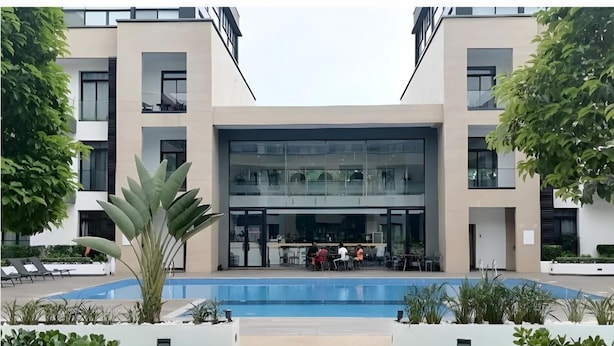 A modern hotel with a central glass facade, outdoor seating area, and a pool. - Embassy Gardens Cantonments Accra (Accra)