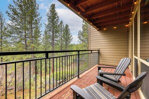 A wooden deck with two Adirondack chairs and a railing, overlooking a forested area.