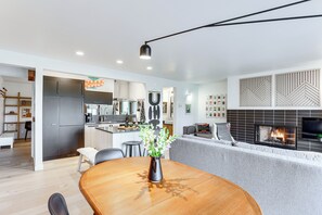 A modern kitchen with a central island, a dining area with a wooden table, and a living area with a fireplace.