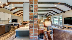 A spacious kitchen with a central island, wooden beams, and a brick accent wall. - Chic Family-friendly Home in Riverside: 7 Mi to KC (Riverside)