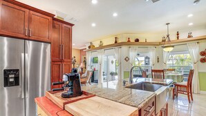 A kitchen with a stainless steel refrigerator, wooden cabinets, a granite countertop, and a large island with a sink. - Near Parks: Port St Lucie Home w/ Private Pool! (Port Saint Lucie)