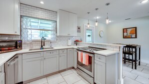 A modern kitchen with white cabinetry, a built-in oven, a microwave, and a large window with a decorative curtain.