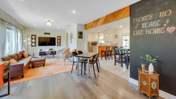 A modern living room with a dining area, a kitchen in the background, and a large blackboard with a motivational quote.