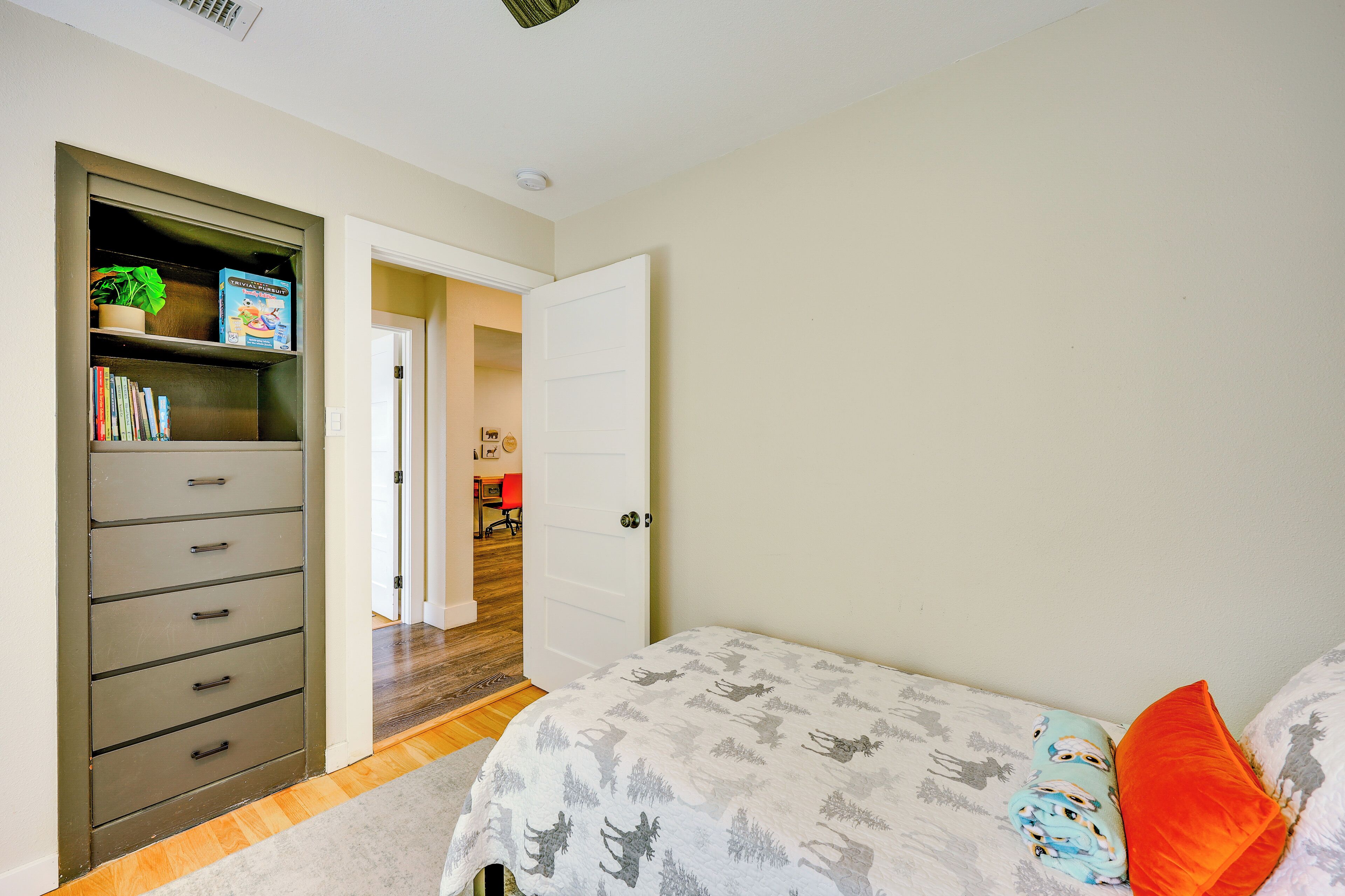 A bedroom with a bed, a dresser, a bookshelf, and a door leading to another room.