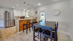 A modern kitchen with a wooden island, stainless steel refrigerator, and a dining area with a blue table and chairs.