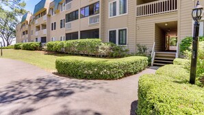 A multi-story residential building with balconies, a well-maintained lawn, and a pathway leading to the entrance.