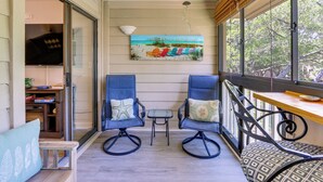 A balcony with two rocking chairs, a small table, and a painting of beach chairs.