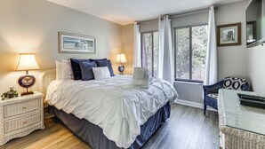 A bedroom with a bed, bedside tables, a chair, a window with curtains, and a wall-mounted TV.