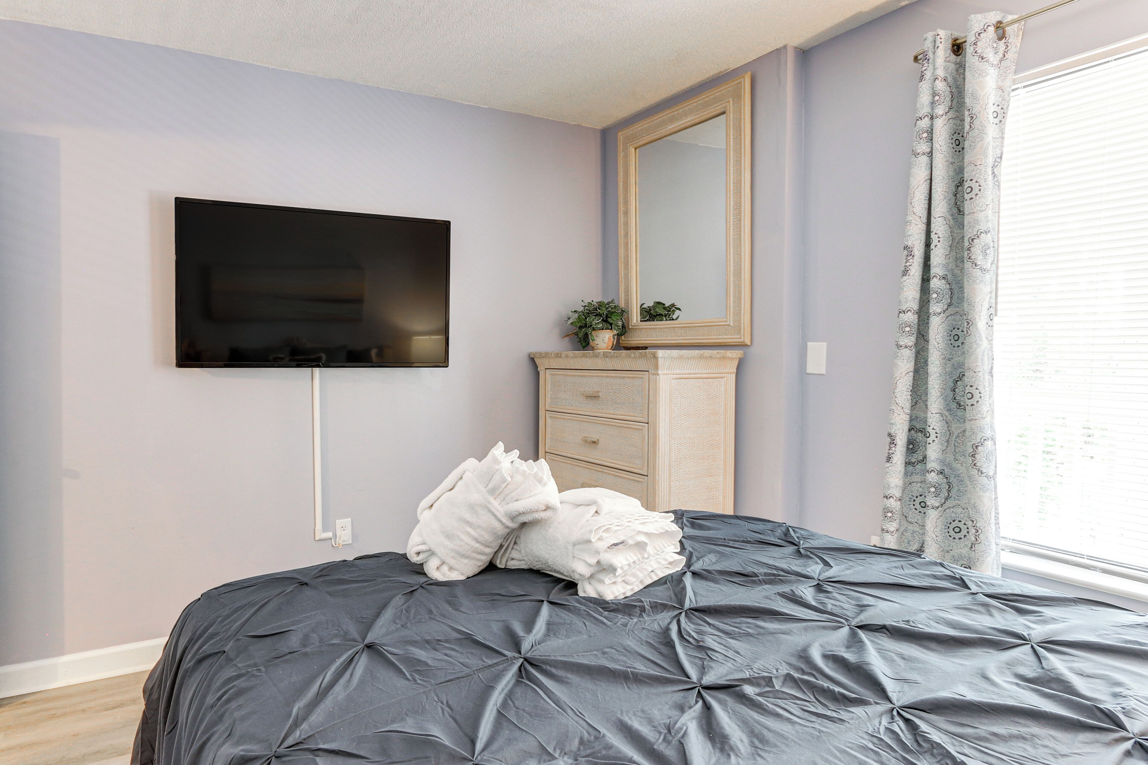 Ein Schlafzimmer mit einem Bett, einem flachbildfernseher an der Wand, einer Kommode und einem Fenster mit Vorhängen.