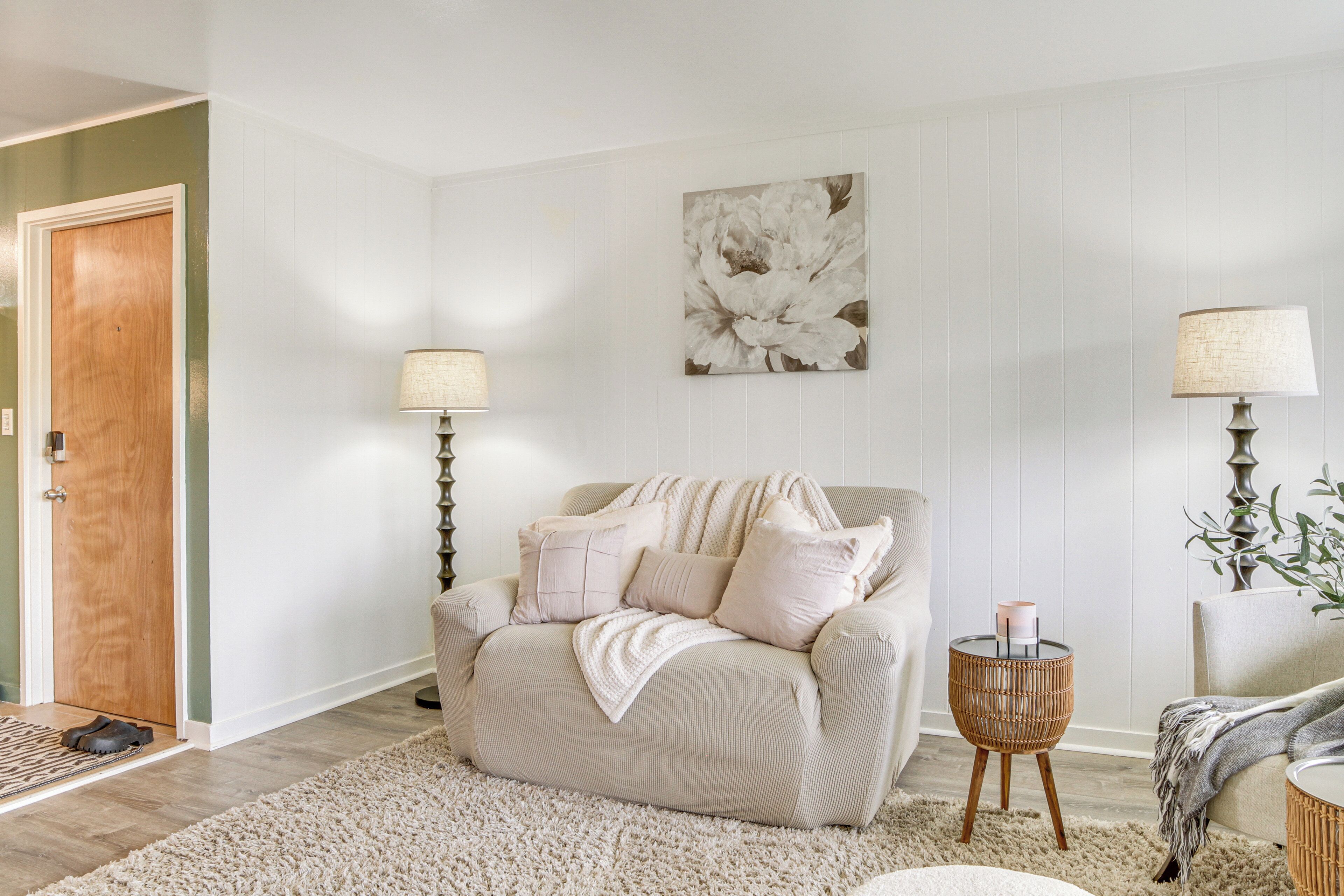 A living room with a beige sofa, two floor lamps, a large floral artwork, and a wooden door.