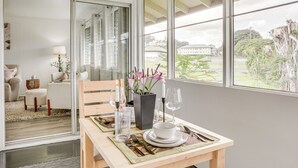 A dining area with a table set for two, a vase with flowers, and a view of the outdoors. - Hilo Apartment w/ Lanai - 2 Mi to Beaches! (Hilo)