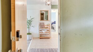 A hallway with a wooden door, a welcome sign, a mirror, a potted plant, and a patterned rug. - Hilo Apartment w/ Lanai - 2 Mi to Beaches! (Hilo)