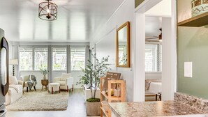 A modern living room with a large window, a sofa, a coffee table, and a potted plant. - Hilo Apartment w/ Lanai - 2 Mi to Beaches! (Hilo)