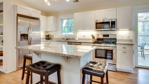 Una cocina moderna con armarios blancos, encimera de granito, electrodomésticos de acero inoxidable y una isla grande con taburetes de bar.