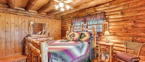 A log cabin bedroom with a bed, wooden walls, a ceiling fan, and a window with shutters.