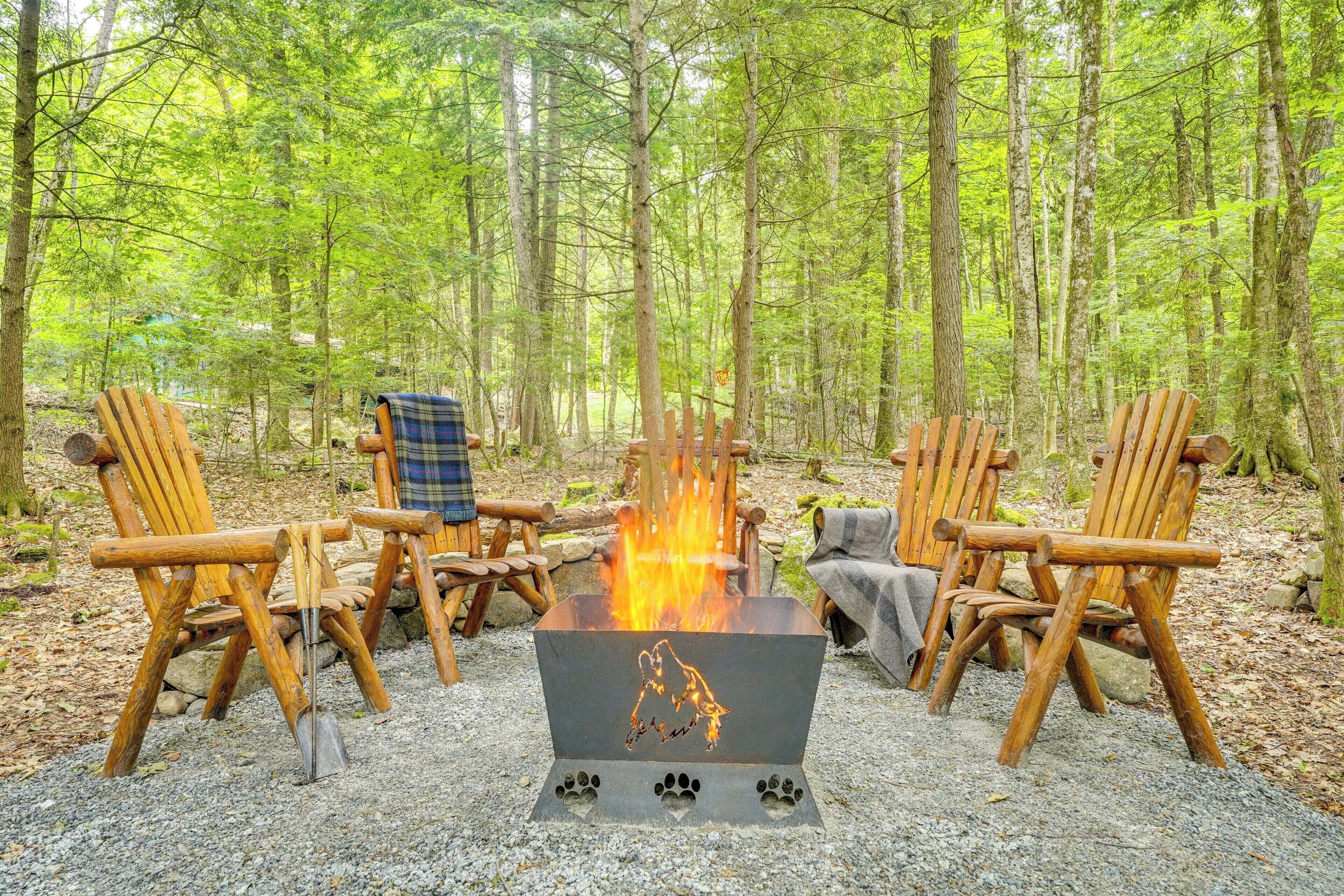 Un feu de camp autour duquel sont disposées quatre chaises Adirondack en bois, le tout dans un cadre forestier.