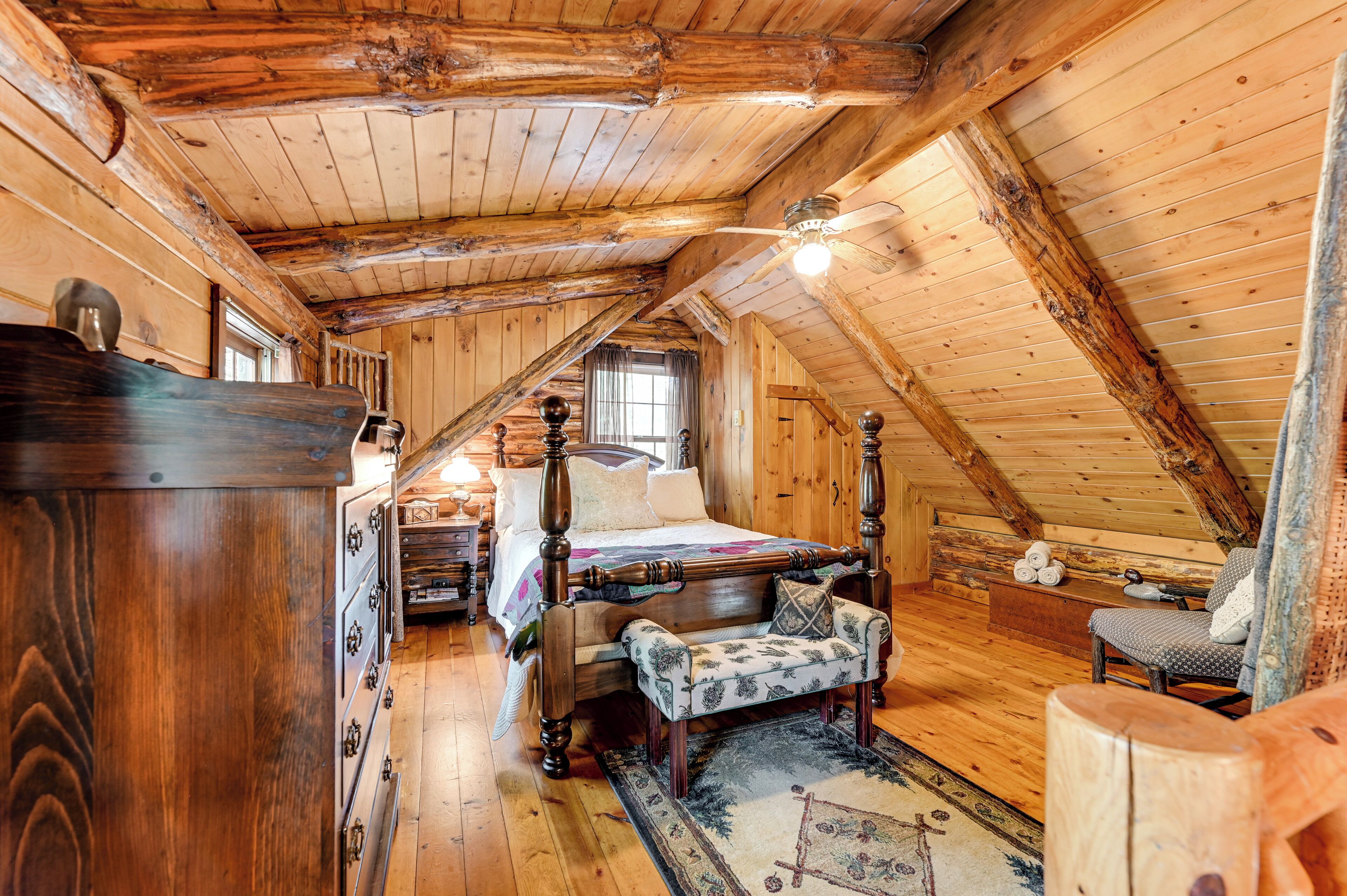 Een slaapkamer in een blokhut met een hemelbed, houten wanden en een schuine kap.
