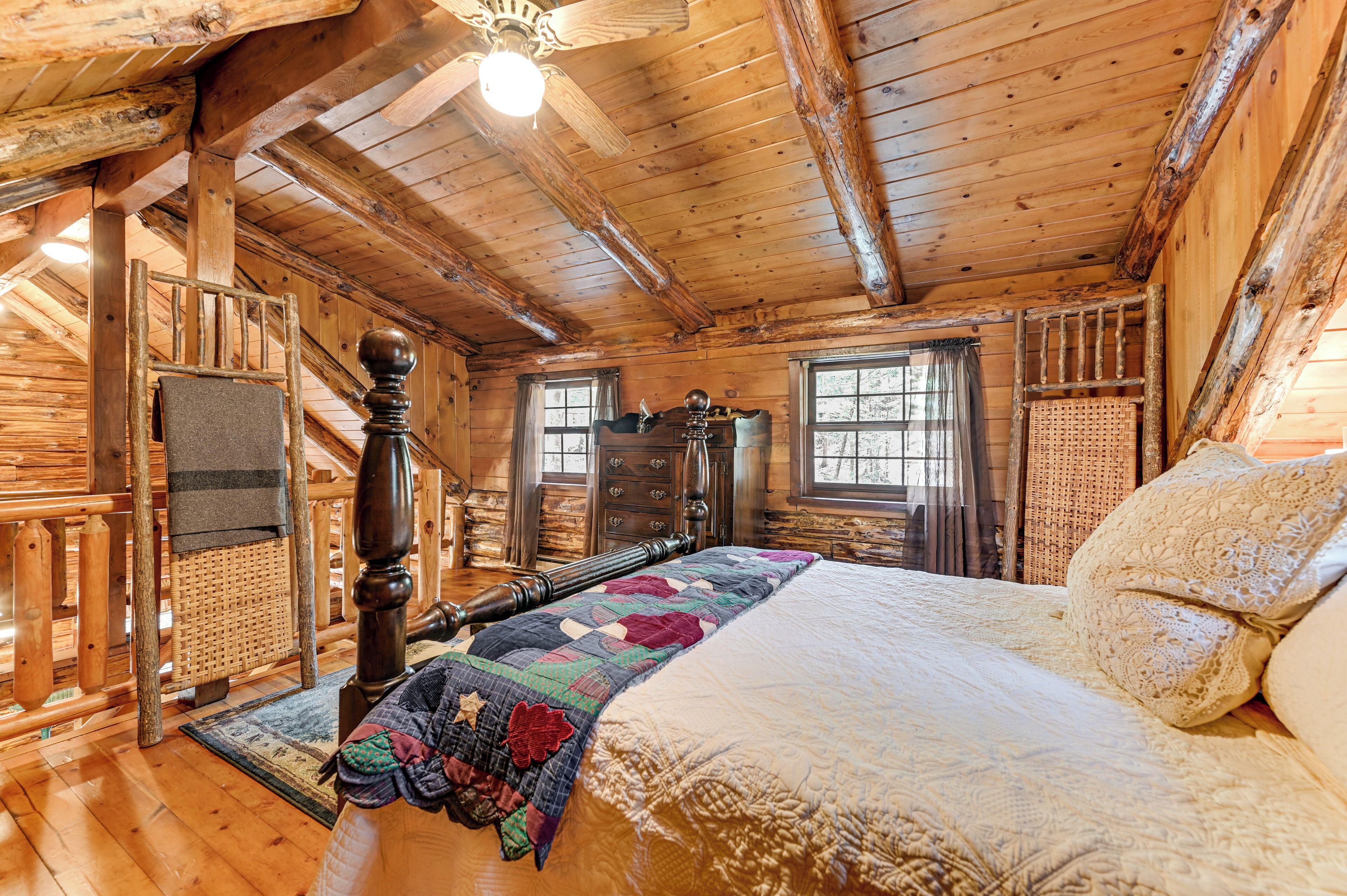 A wooden cabin bedroom with a large bed, a wooden headboard, a wooden floor, and a ceiling fan.
