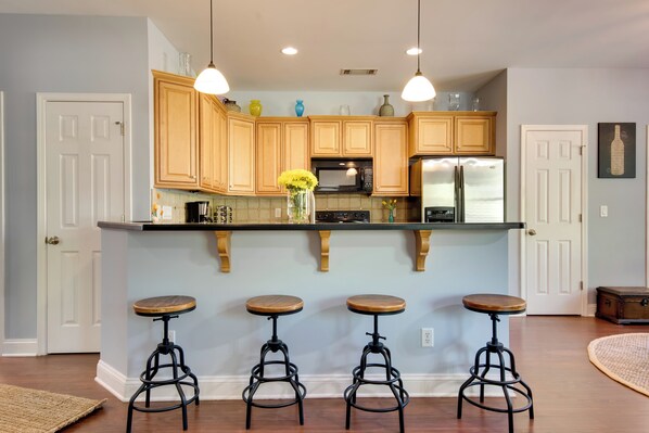 Una cocina con armarios de madera, una isla central con taburetes y un refrigerador.