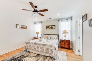 Une chambre à coucher avec un lit, des tables de chevet, un ventilateur de plafond et une porte.