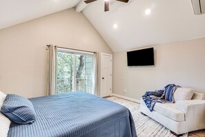 Ein Schlafzimmer mit Bett, Sessel, Fernseher und einem Fenster mit Vorhängen.