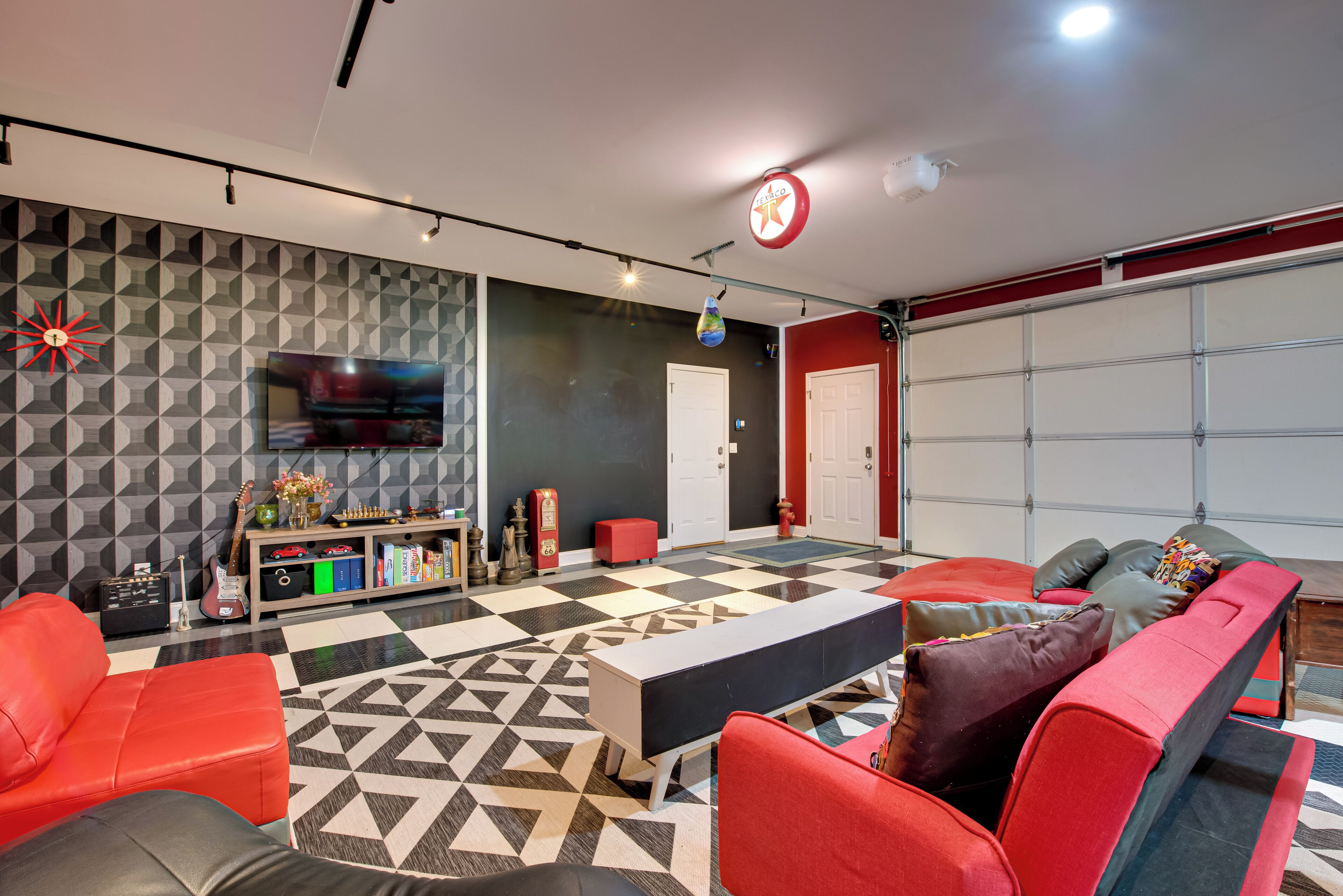 Un salon moderne avec un sol à motifs géométriques, des meubles rouges et noirs, une bibliothèque remplie de divers objets et un téléviseur fixé au mur.