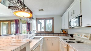 A kitchen with white cabinets, a stove, a microwave, and a window with curtains. - Ski-in/ski-out Wintergreen Resort Condo + Hot Tub! (Nellysford)