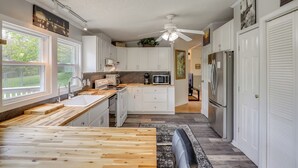 Eine moderne Küche mit weißen Schränken, einer Holz Arbeitsplatte, einem Deckenventilator und einem Kühlschrank.