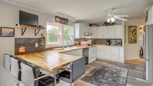 Eine moderne Küche mit Holztischplatte, weißen Schränken, einem eingebauten Backofen und einem Deckenventilator.