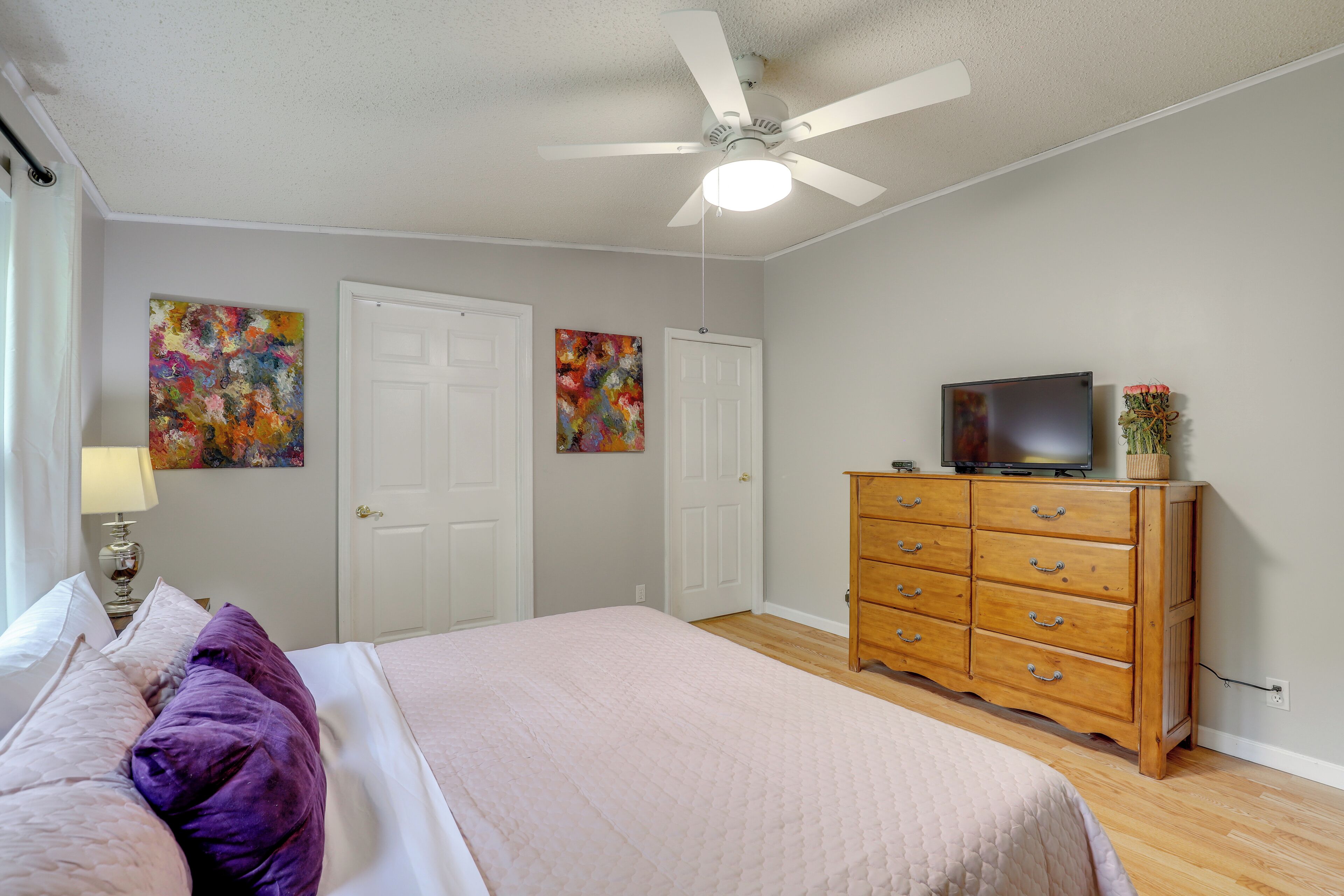 Une chambre à coucher comprenant un lit, une commode, un ventilateur de plafond et deux portes.