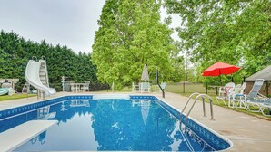 A swimming pool with a slide, surrounded by trees and a fenced area with lounge chairs and umbrellas. - Pet-friendly Georgia Home w/ Pool Access! (Cleveland)