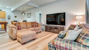 A living room with a sofa, ottoman, and a television. There is a wooden cabinet and a lamp. - Pet-friendly Georgia Home w/ Pool Access! (Cleveland)