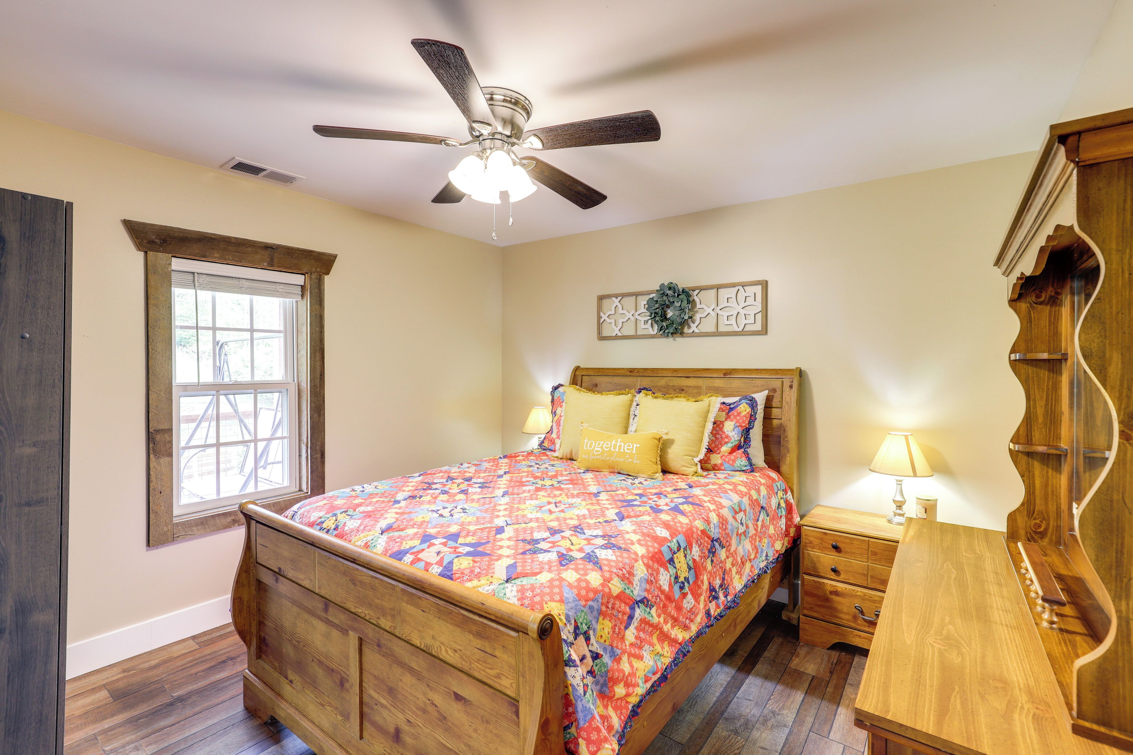 A bedroom with a wooden bed, a ceiling fan, a window, a nightstand, and a dresser.