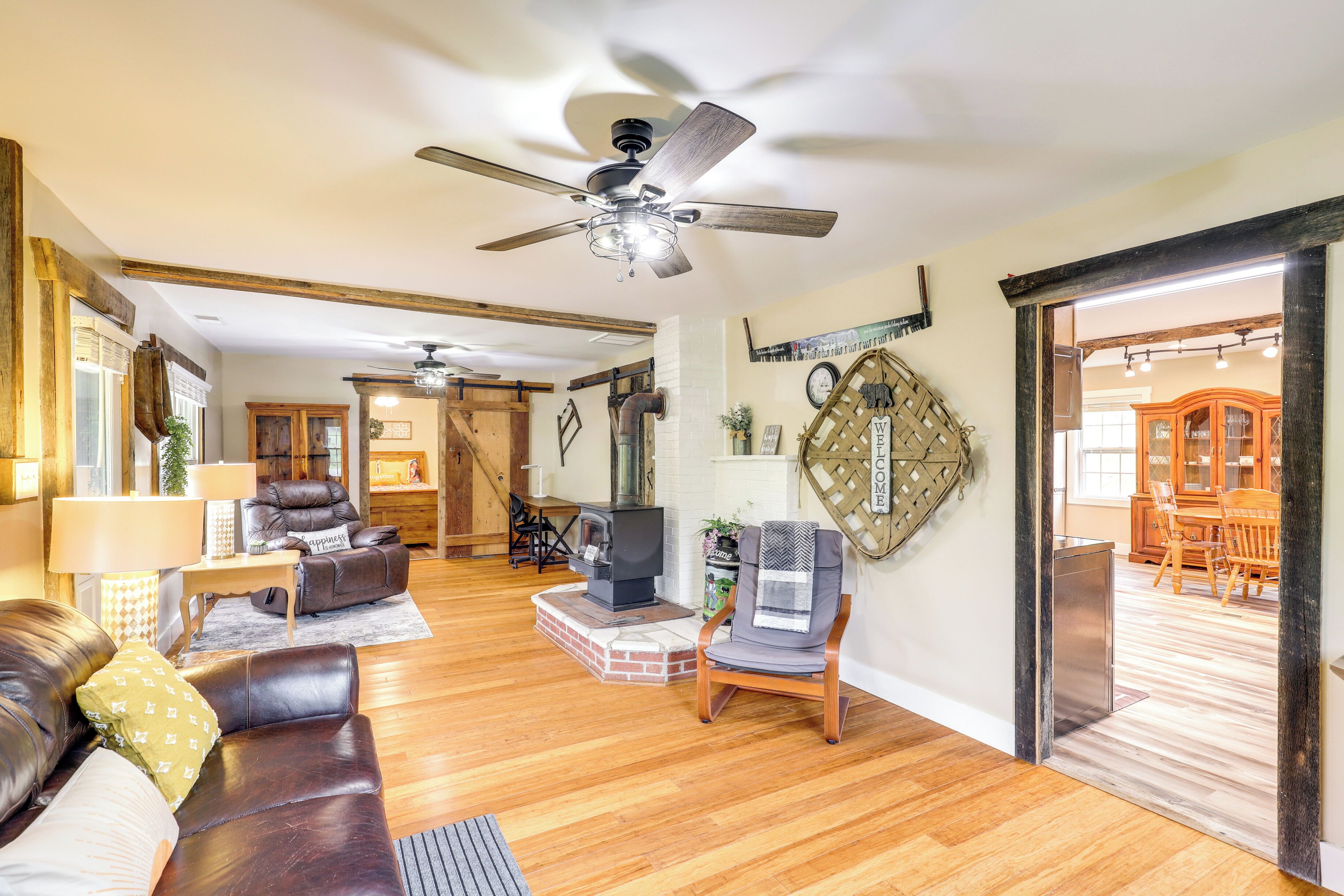 A spacious living room with a fireplace, leather sofas, a dining area, and a ceiling fan.