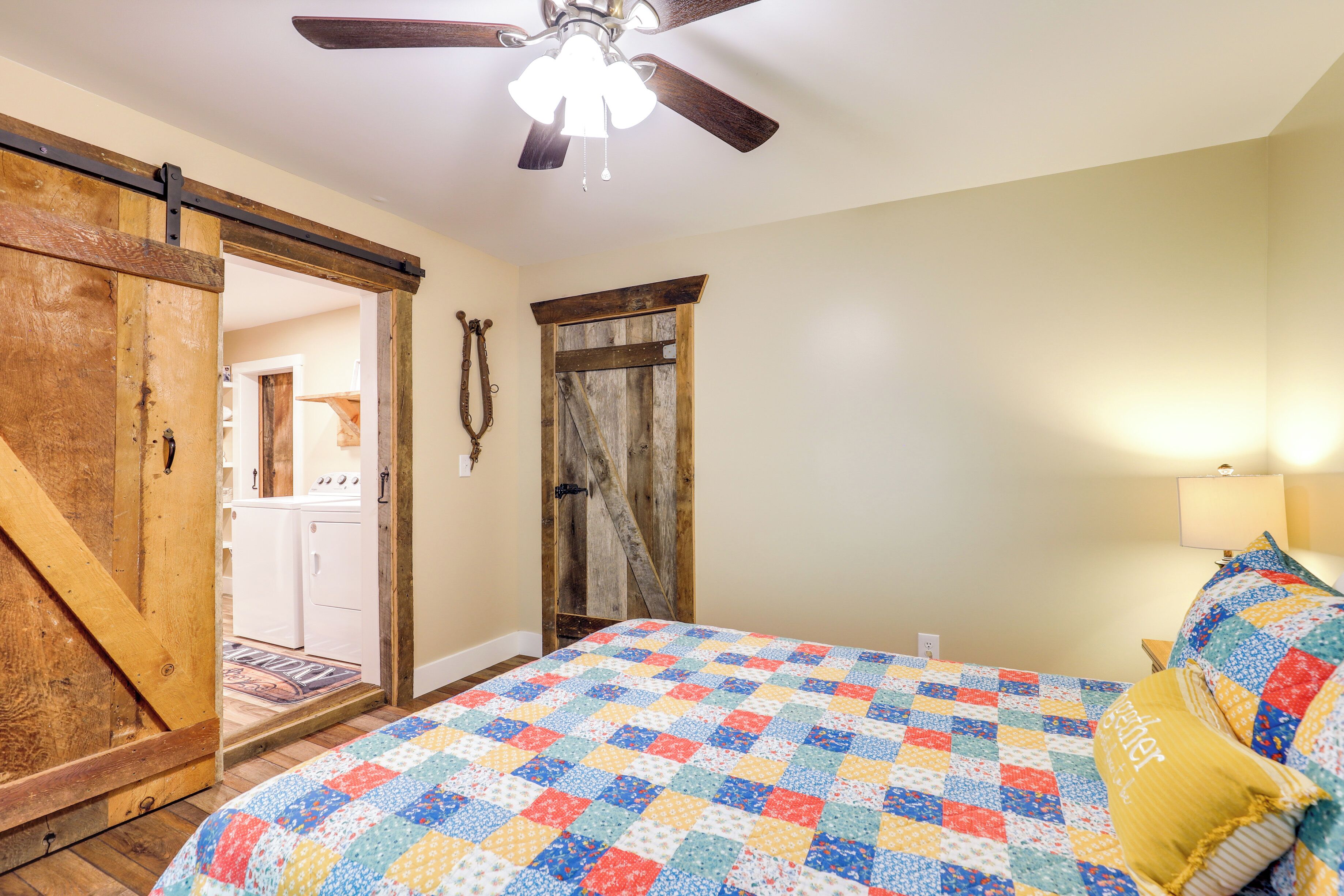 A bedroom with a quilted bedspread, a ceiling fan, and a wooden door.