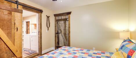 A bedroom with a quilted bedspread, a ceiling fan, and a wooden door.
