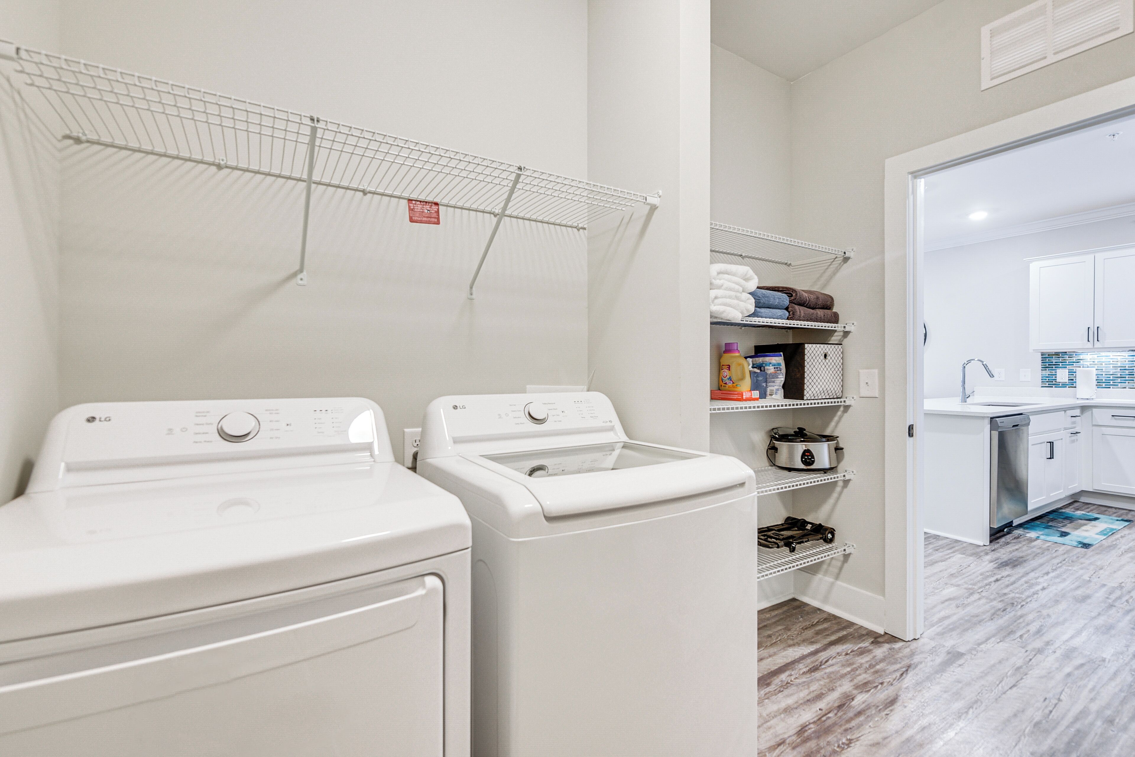 A laundry area with two white washers and dryers, a drying rack, and a kitchen area with a sink and cabinets.