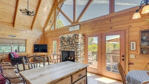 Interior de uma cabana de madeira com lareira de pedra, mesa de jantar em madeira e televisão na sala de estar.