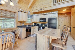 Une cuisine rustique aménagée dans une cabane en bois, avec une table à manger, des chaises et un réfrigérateur.