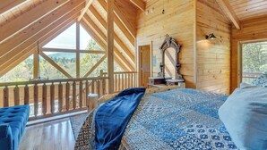 Quarto de cabana de madeira com uma cama grande, um ventilador de teto e vista para o exterior.