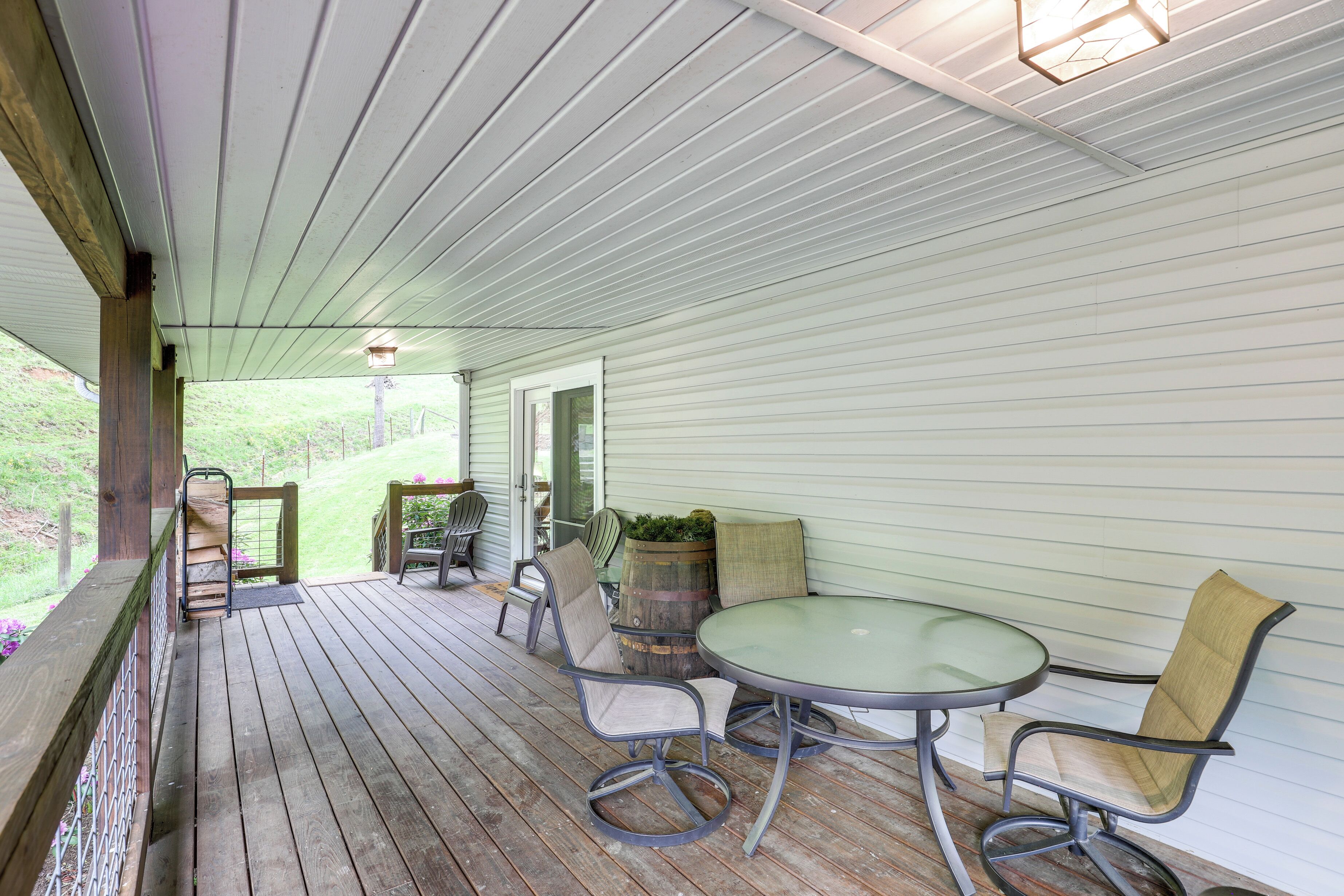 A covered porch with a round table and chairs, a wooden railing, and a view of the outdoors.