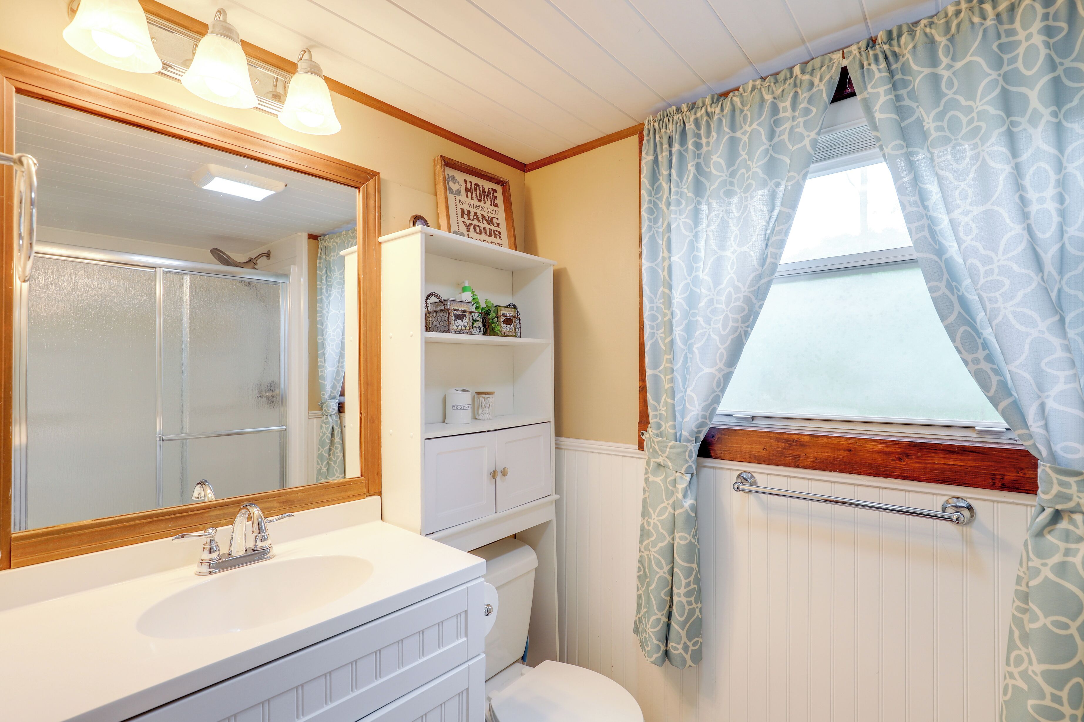 Een badkamer met een wit wastafel, spiegel en toilet. Er is een plank met toiletartikelen en een handdoekhouder.