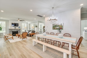 A spacious dining area with a long wooden table, benches, and wicker chairs. - Cape Charles Home: Private Pier & Beach-front Deck (Cape Charles)